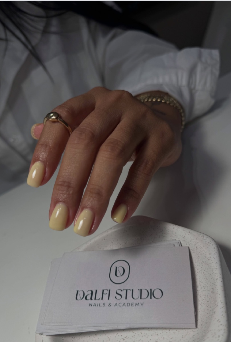 Mano con manicura butter yellow y anillos dorados